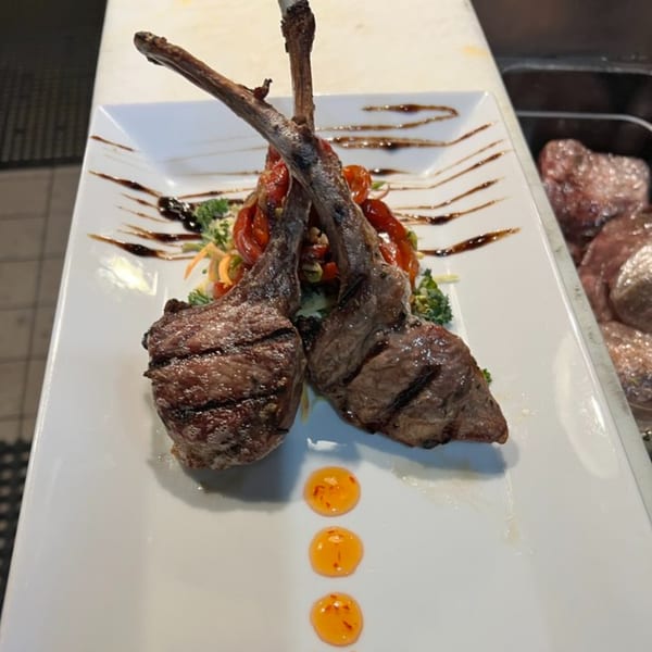 Two grilled lamb chops with vegetables and sauce on a white rectangular plate.