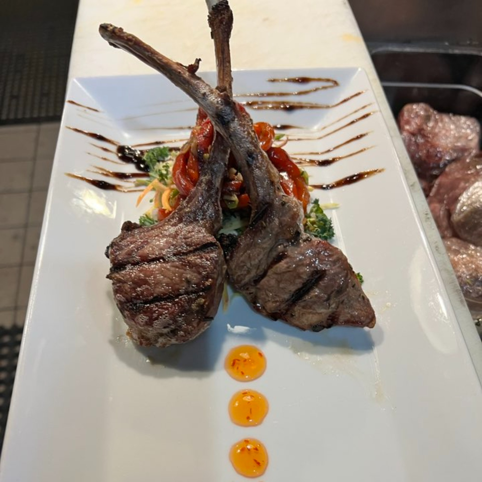 Two grilled lamb chops with vegetables and sauce on a white rectangular plate.
