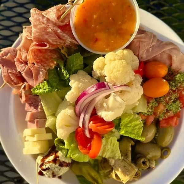 Antipasto salad with meats, cheeses, olives, vegetables, and dressing on a white plate.