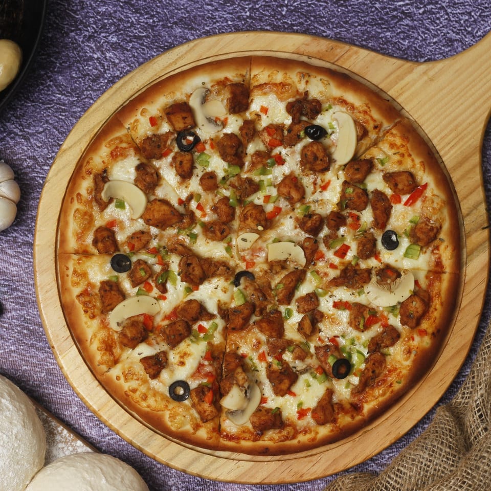 Philly Pizza Authority's chicken pizza, topped with mushrooms, olives, and bell peppers on a wooden board.
