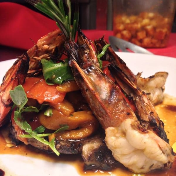 Grilled shrimp and vegetables with rosemary garnish on a white plate with sauce.